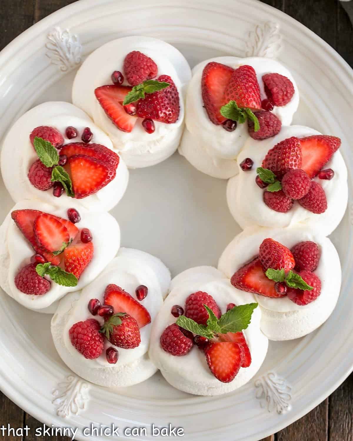 Overhead view of a Christmas Pavlova on a white plate topped with cream, berries and mint.