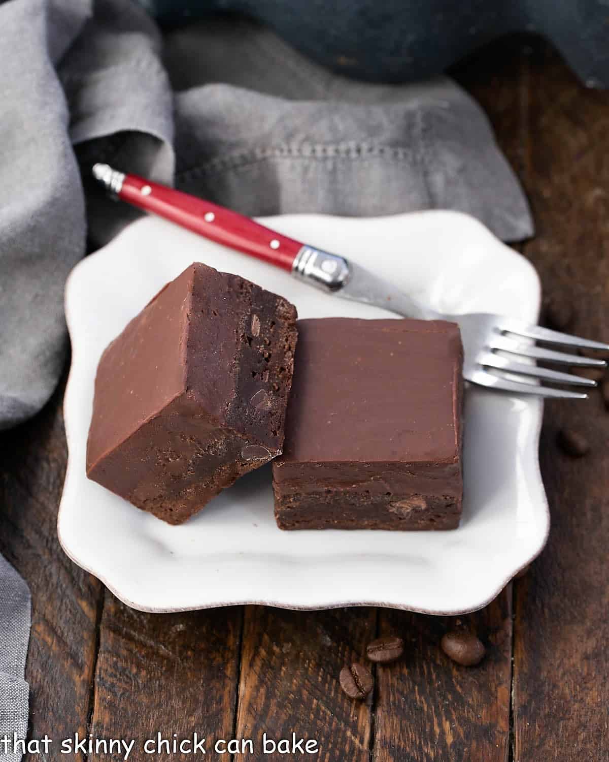 Two kalua fudge topped brownies on a square white plate with a red handle fork.
