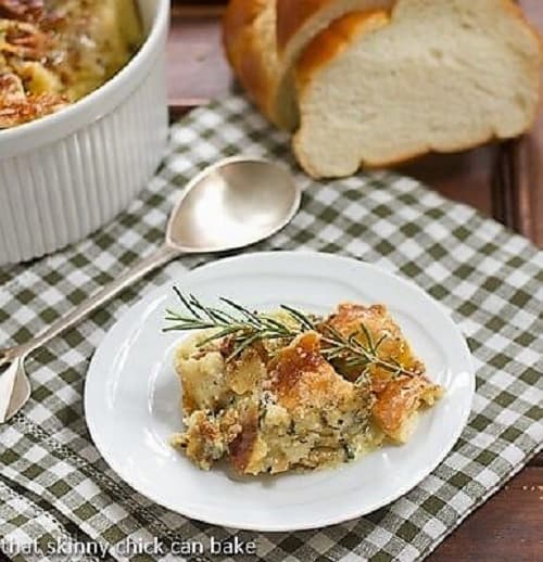 Breakfast strata on a white plate with a sprig of rosemary