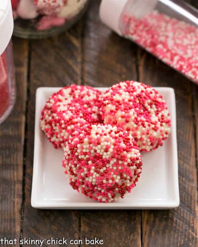 3 sprinkle cookies with red and pink sprinkles on a square white plate.