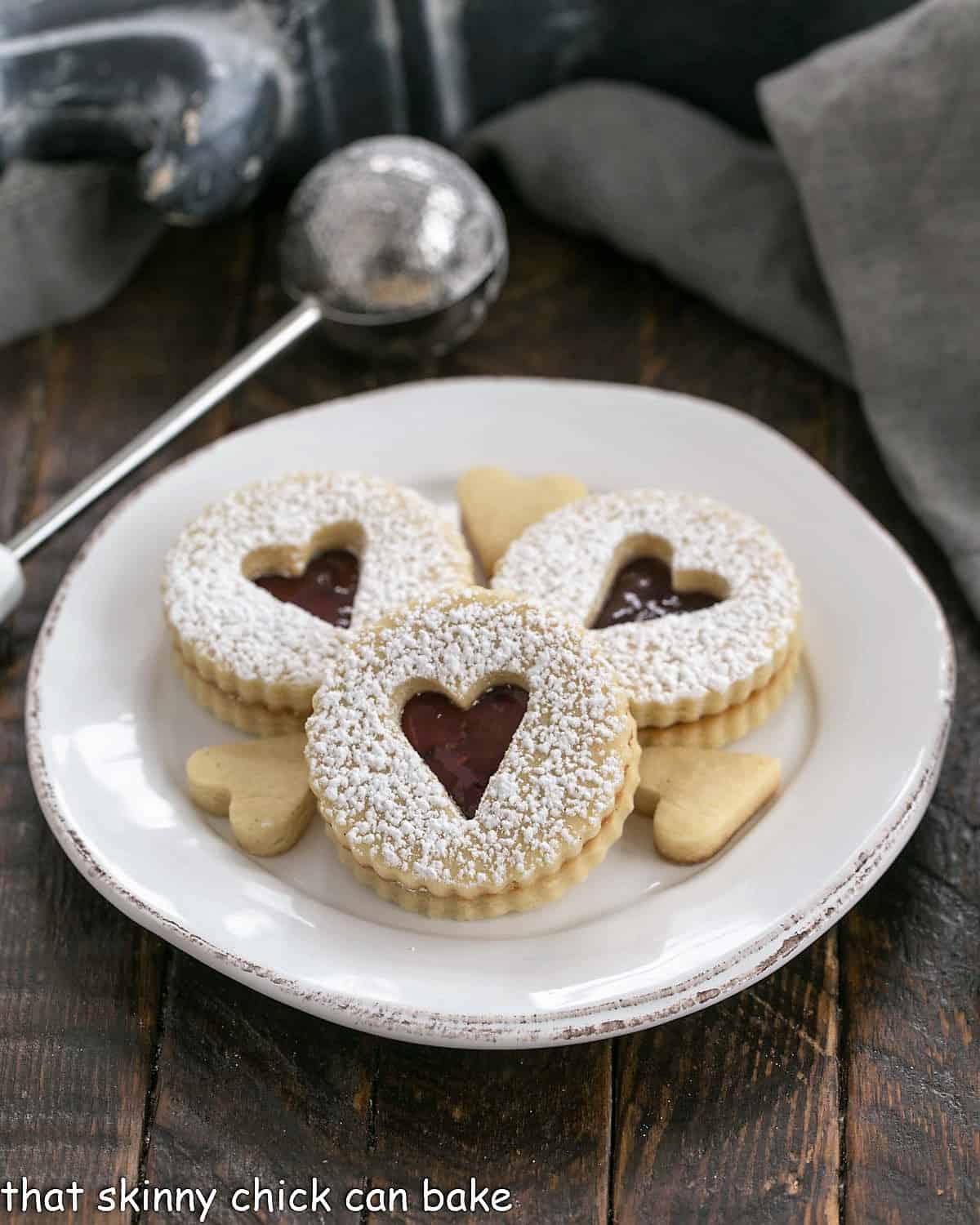 3 linzer cookies dusted with powdered sugar on a round white dessert plate.