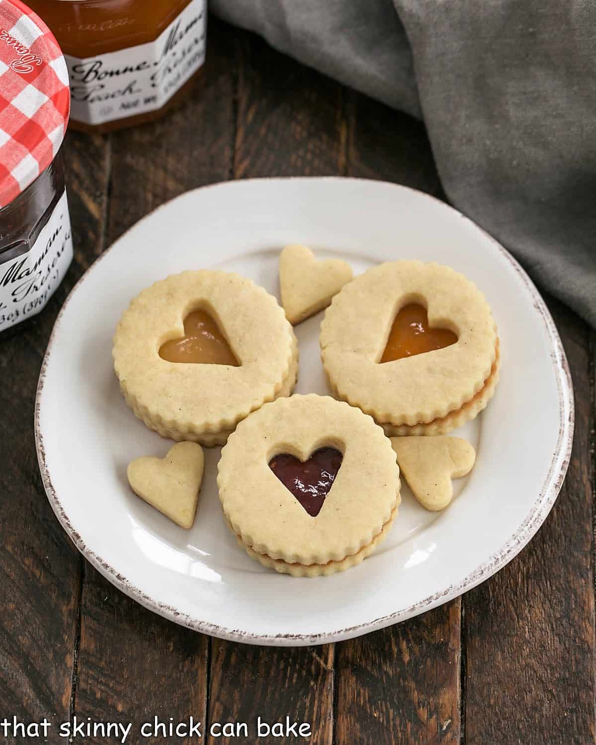 Overhead view of 3 linzer cookies and their cutouts on a round white plate.