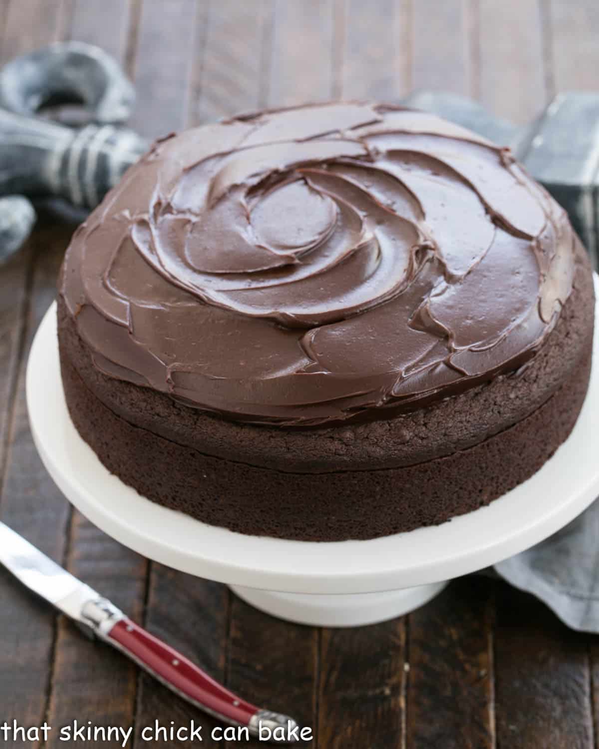 One layer chocolate cake with ganache frosting on a white cake stand.