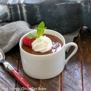 A teacup full of chocolate pots de creme with a raspberry and whipped cream garnish.