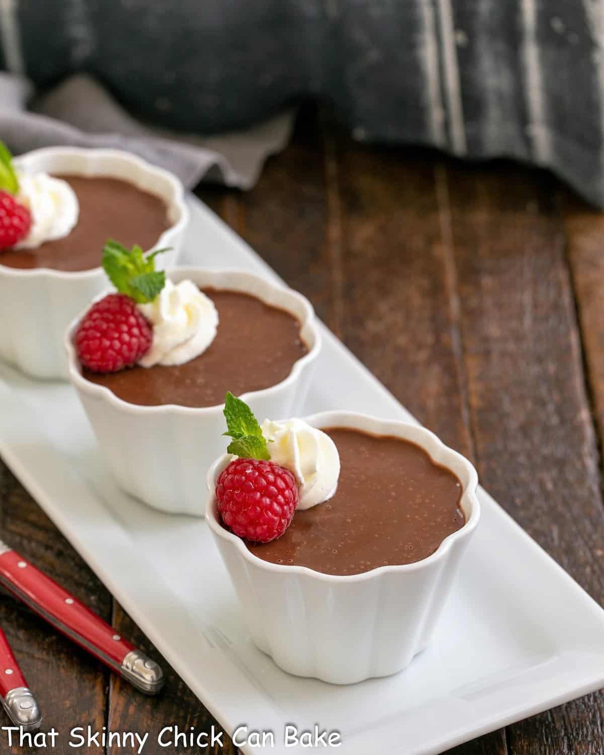 Pots de creme on a white ceramic tray with red handled spoons.