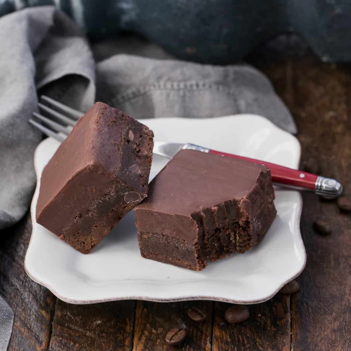 Fudge topped kahlua brownies on a square white plate with a red handled fork.