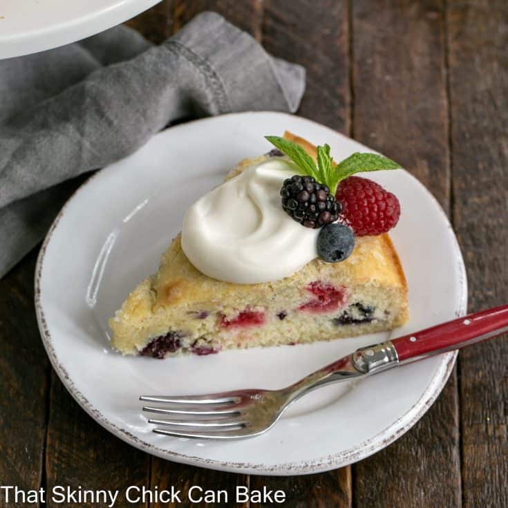 Slice of mixed berry cake on a white plate topped with lemon cream and fresh berries