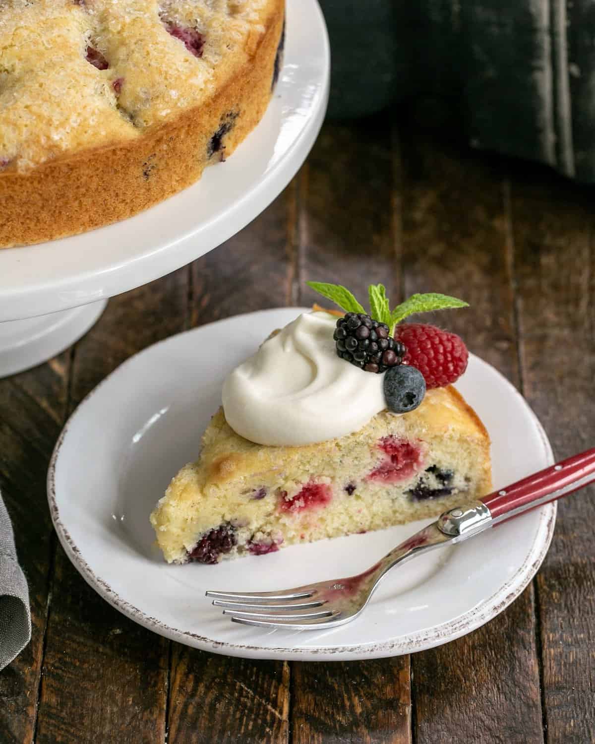 slice of berries cake on a white plate with a red handle fork.