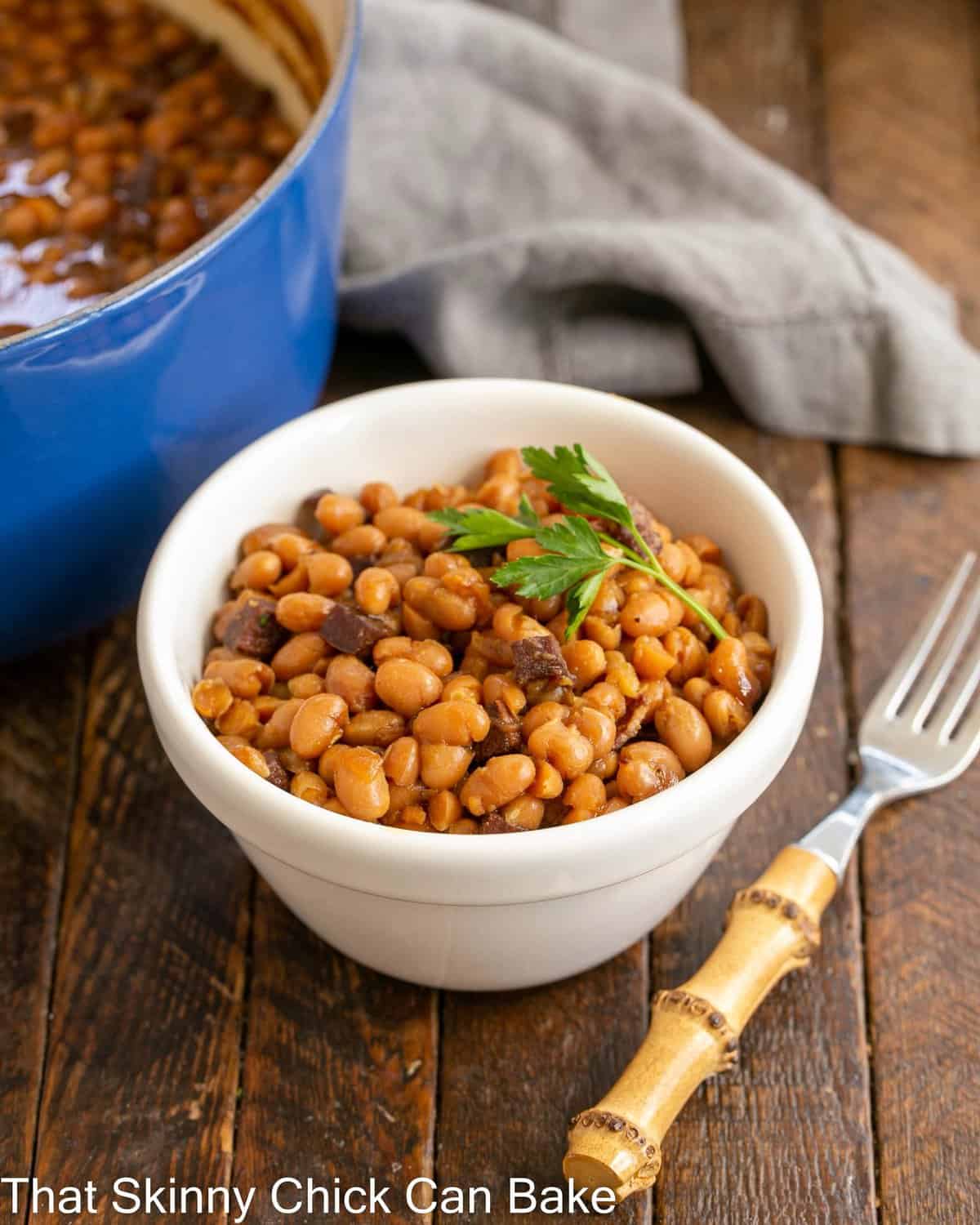 Bowl of boston baked beans in a white bowl with a bamboo fork.