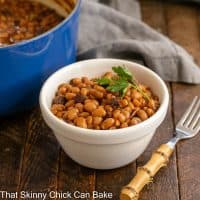 small white bowl filled with baked beans in front of a blue Dutch oven filled with beans