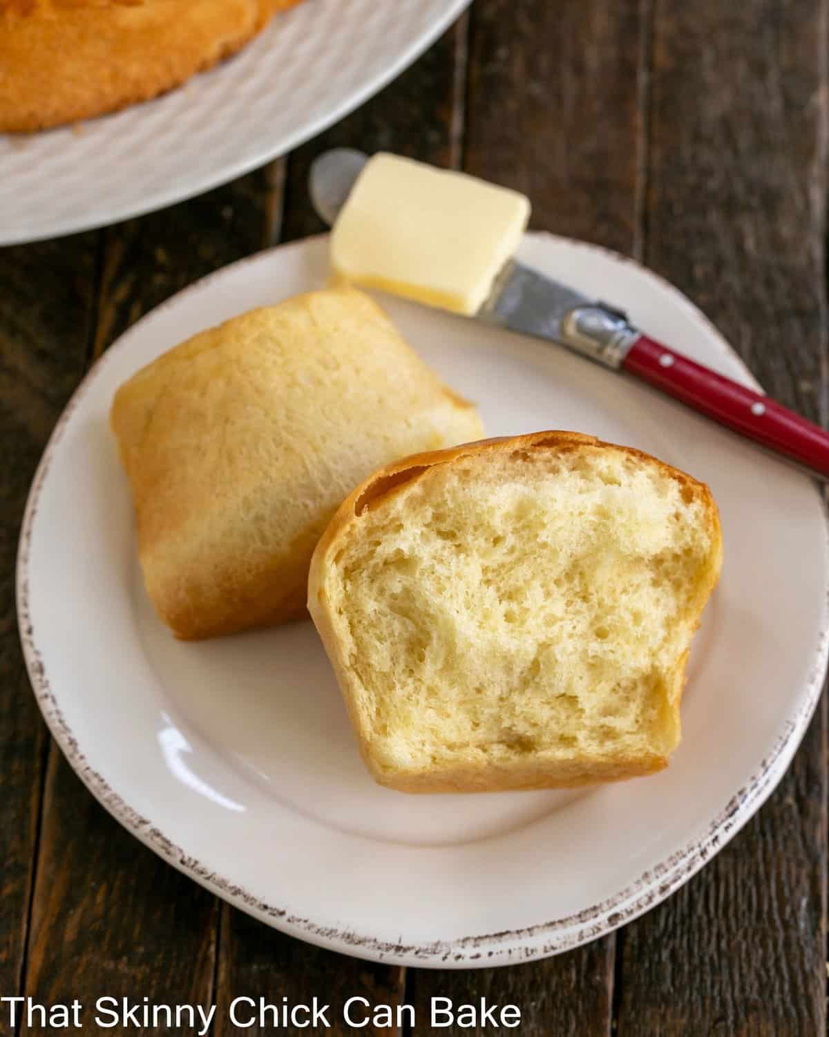 A Japanese Milk Bread Bun torn in half on a small white plate with a red butter knife.