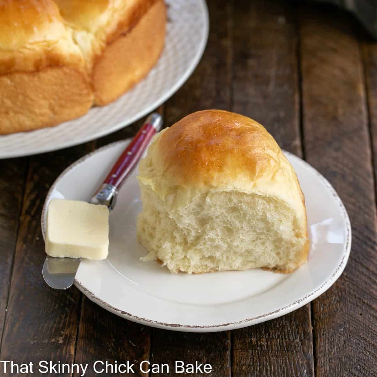 One Japanese Milk Bread Roll on a white plate with a red handled knife with a pat of butter.