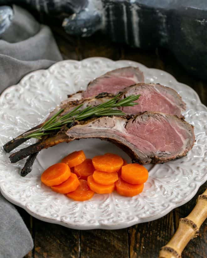 Overhead view of lamb chops on a white decorative plate with a sprig of rosemary and carrot coins