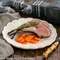 Two marinated lamb chops on a white dinner plate with rosemary garnish and carrots