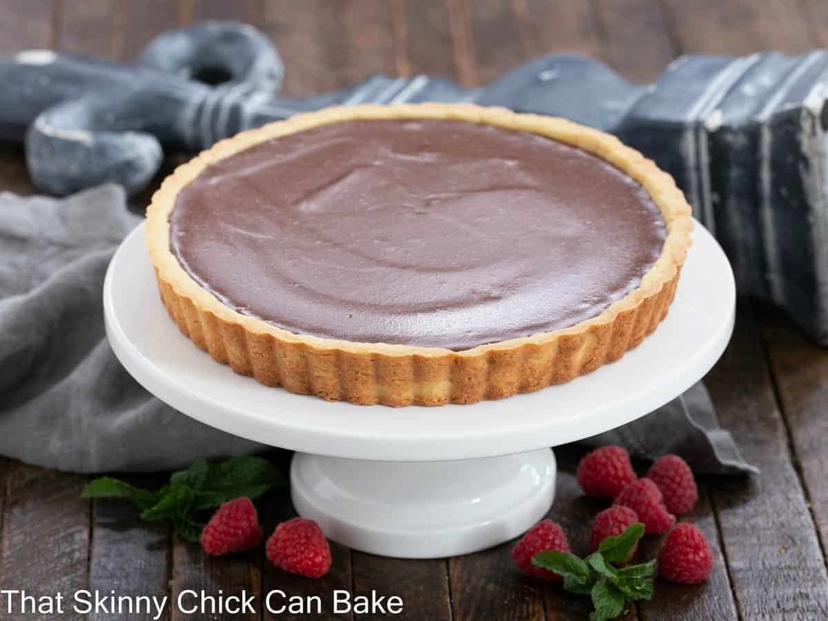 Whole milk chocolate tart on a white cake stand.