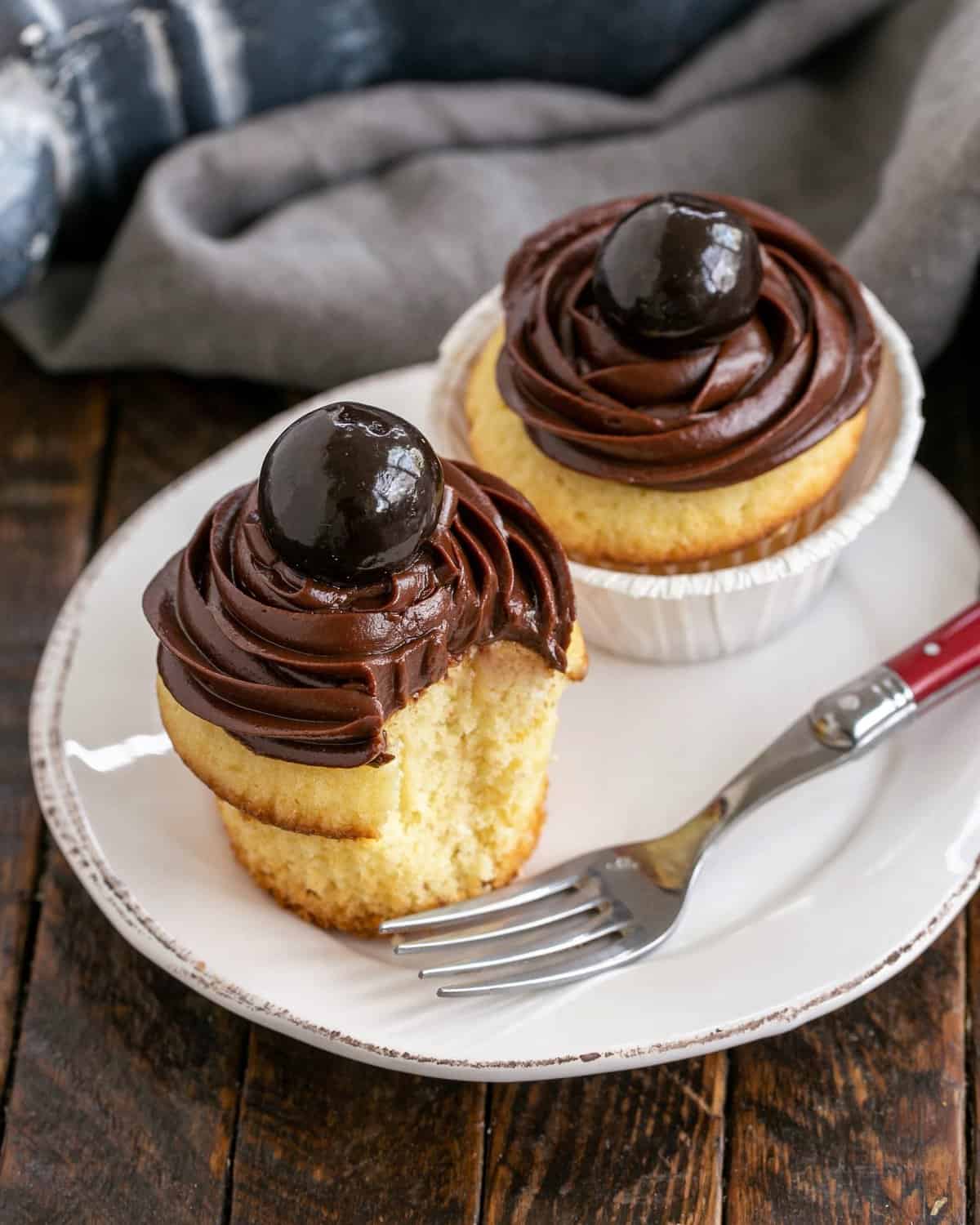 2 yellow cupcakes on a white plate with a red handled fork. 