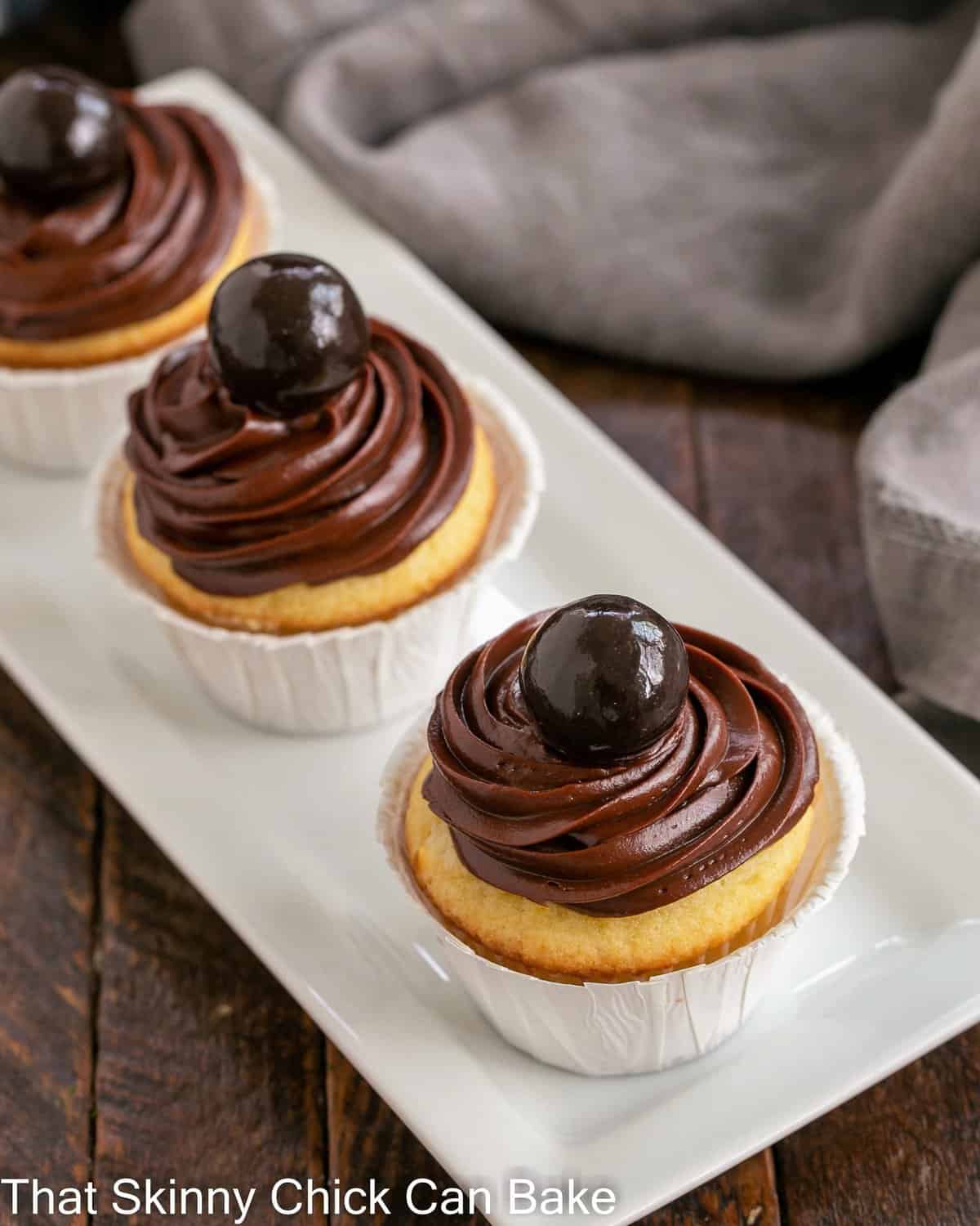 3 yellow cupcakes with chocolate ganache frosting on a white ceramic tray.