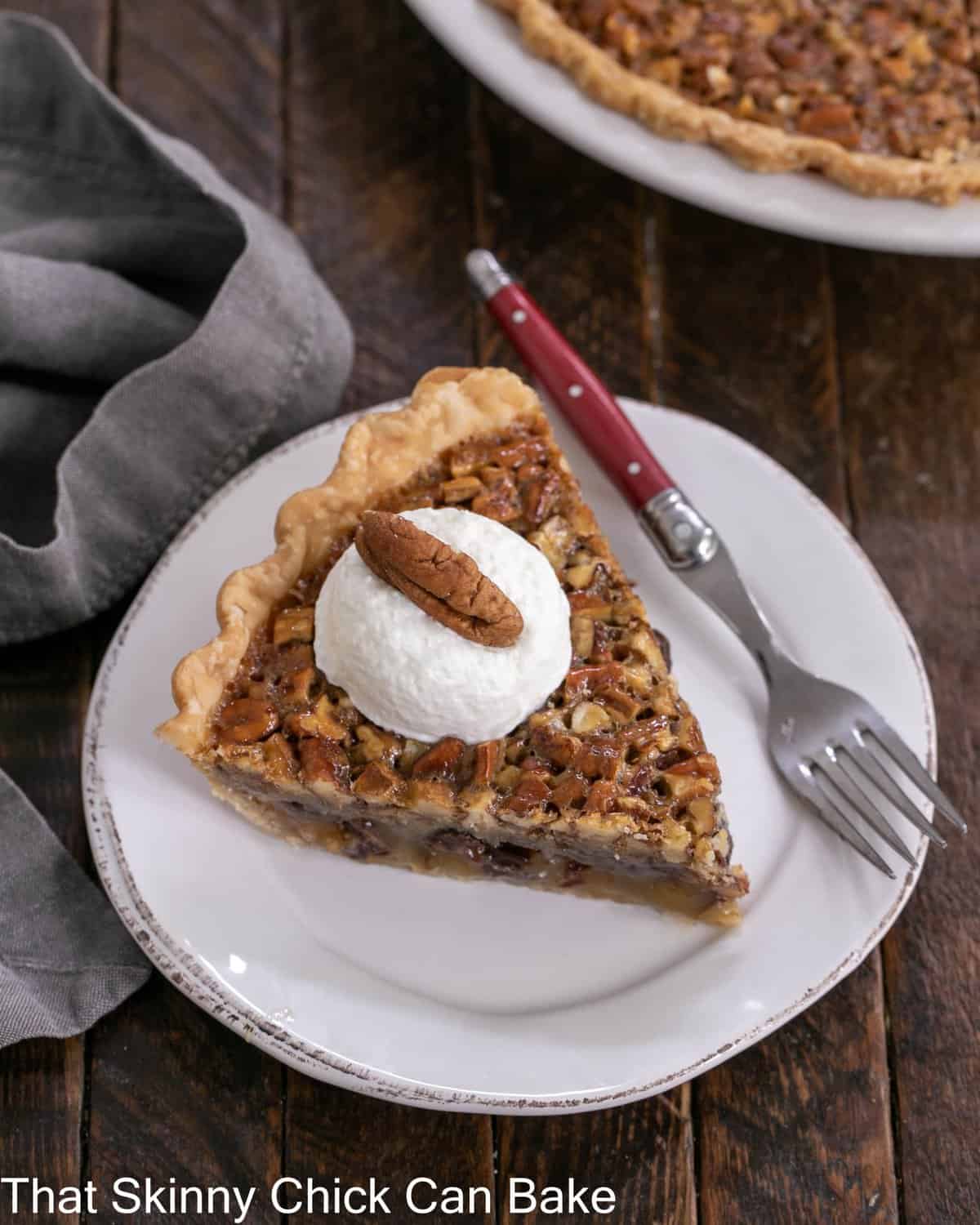 Overhead view of a slice of derby pie topped with whipped cream and a pecan on a white dessert plate