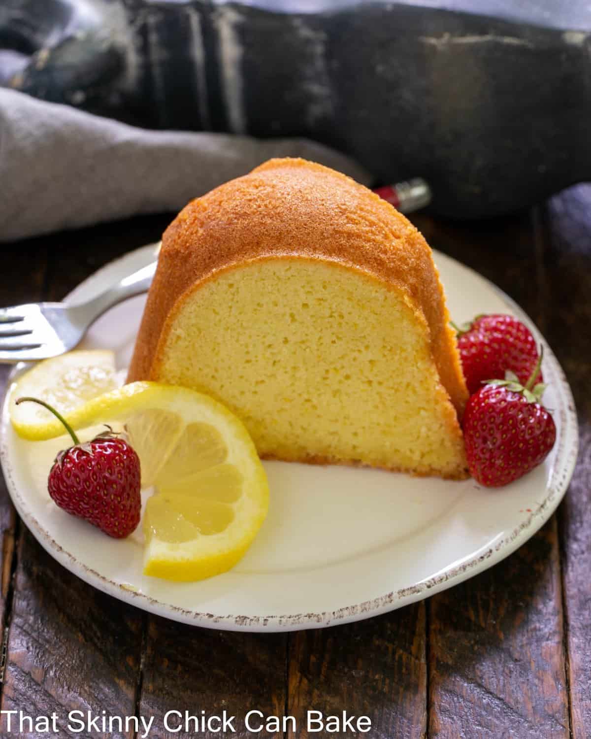 A slice of lemon pound cake on a white dessert plate with fresh strawberries.