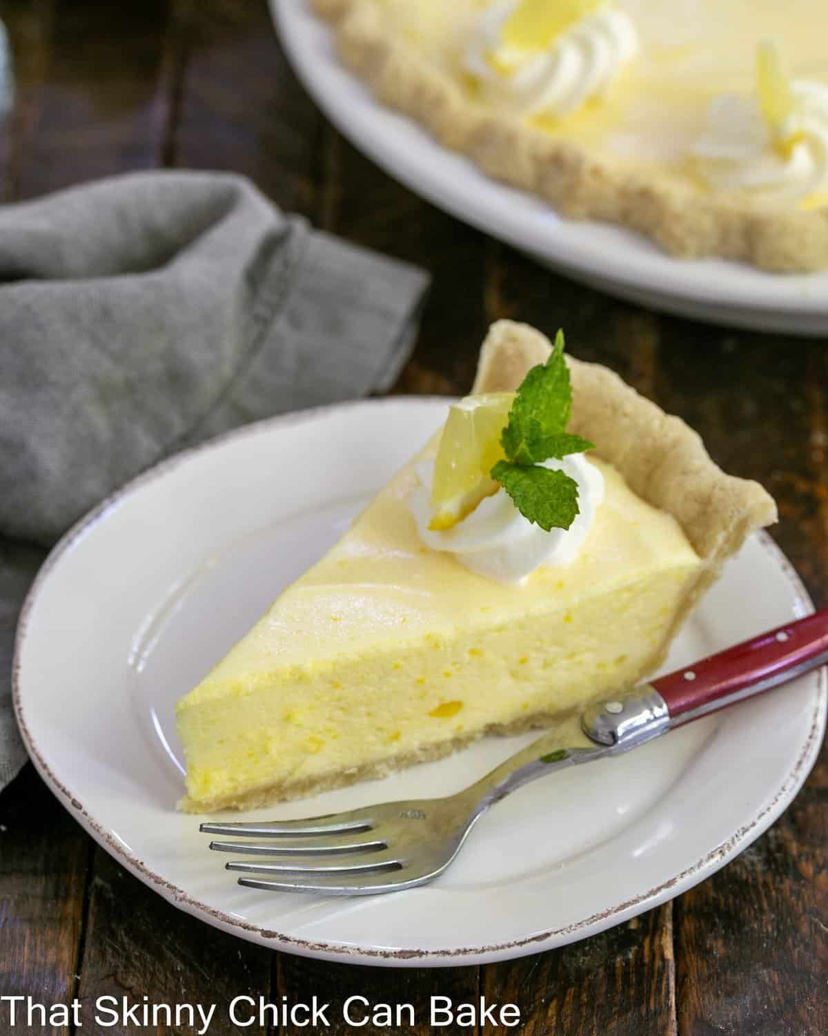 Slice of lemon chiffon pie on a white dessert plate with a swirl of whipped cream and mint sprig garnish.