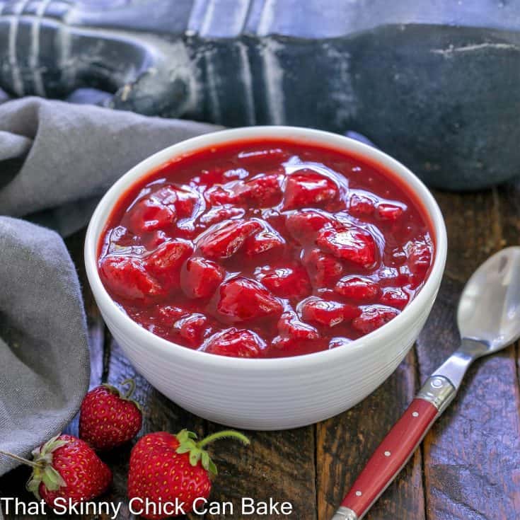 Fresh strawberry compote in a white bowl with a red handle spoon to the side