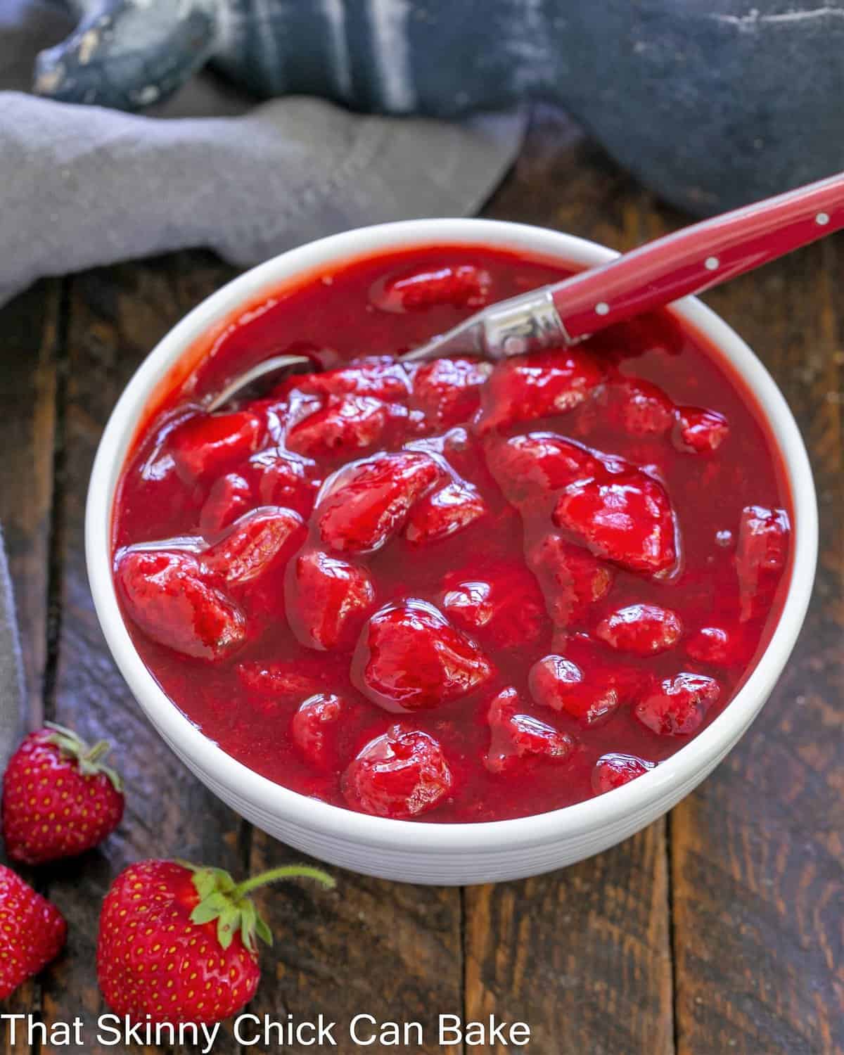 Overhead view of fresh strawberry sauce in a white bowl with a spoon.