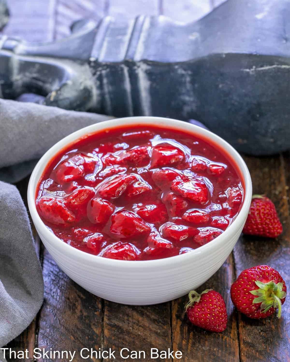 A white bowl full of strawberry sauce with a few fresh strawberries on the side.