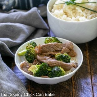 Beef and Broccoli in a small white bowl in front of a bowl of rice