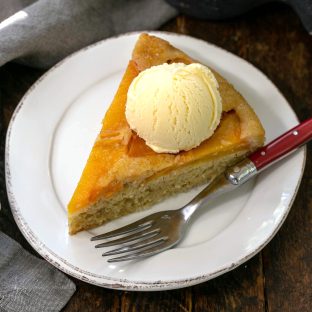 Overhead view of a slice of peach upsidedown cake with a scoop of vanilla ice cream on a white plate with a red handled fork