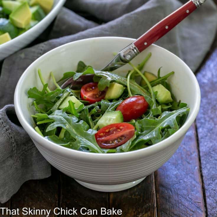 Simple arugula salad in a small white bowl with a fork