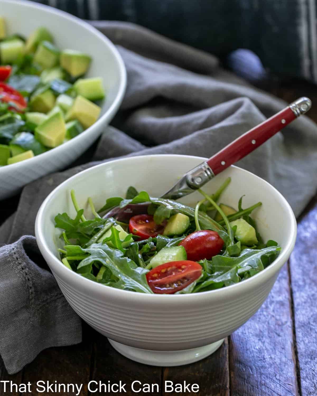 Salad bowl with arugula salad and a red handle fork in front of serving bowl.