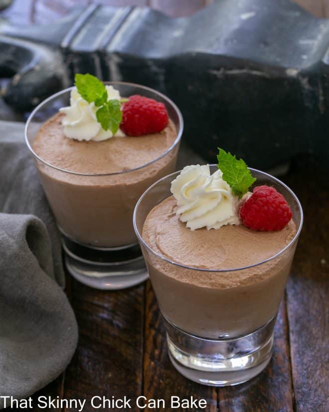 2 dishes of chocolate mousse garnished with whipped cream, raspberries and mint