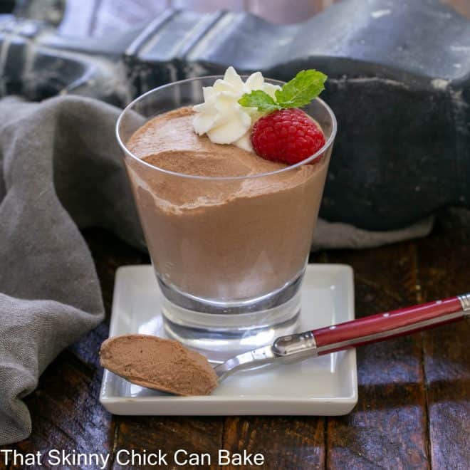 A serving of chocolate mousse in a glass with a spoonful removed on a red handled fork