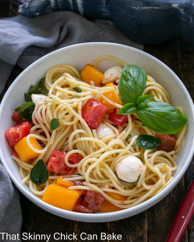 Serving bowl of fresh tomato basil pasta with a basil garnish.