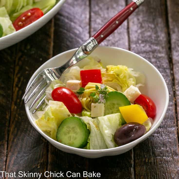 Small white bowl of Greek salad with a red handled fork