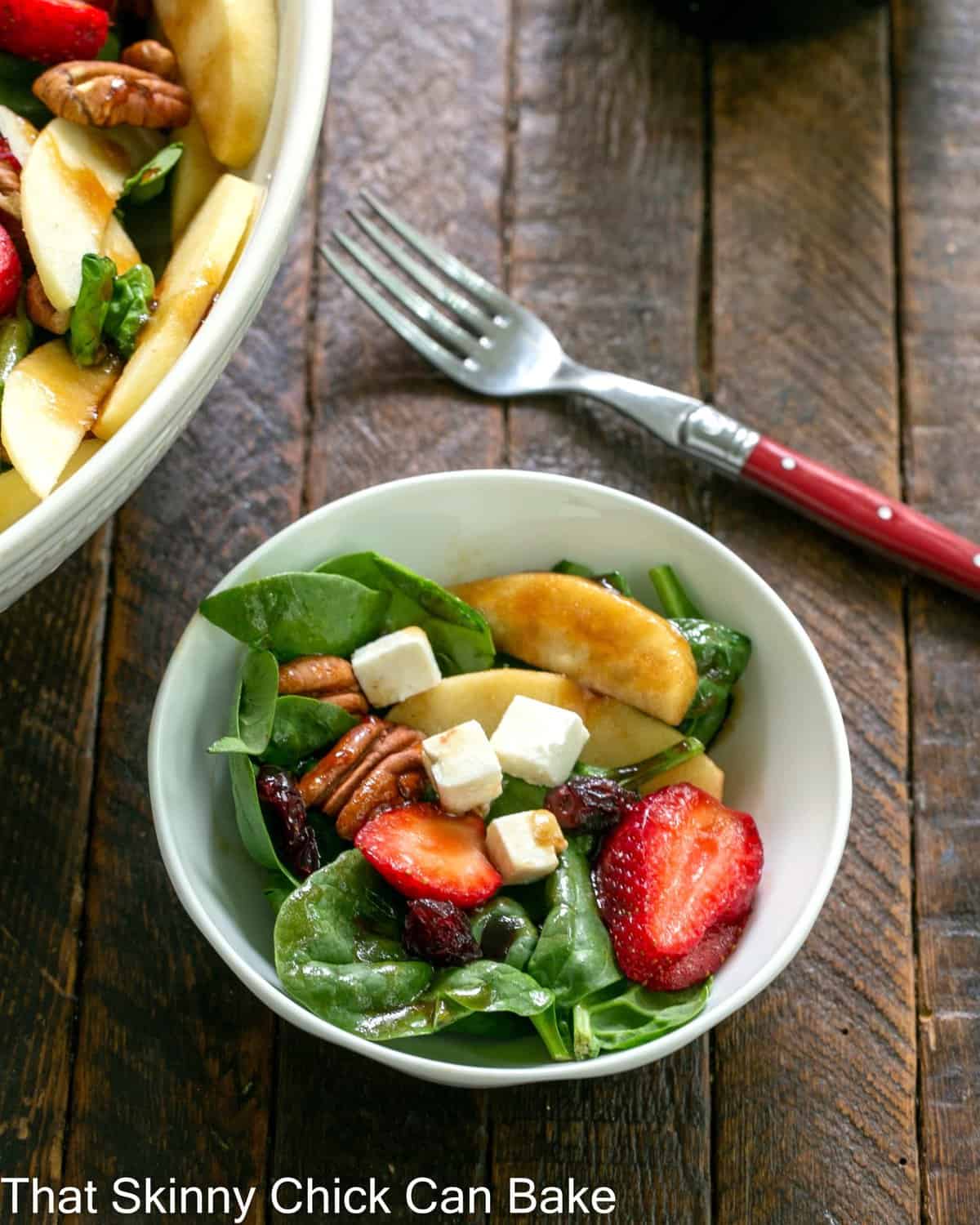 Overhead view of a small bowl of strawberry salad with feta with a red handle fork.