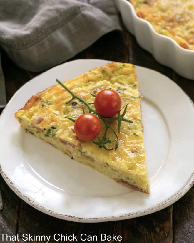 Slice of Zucchini Quiche with Prosciutto garnished with cherry tomatoes on a white plate