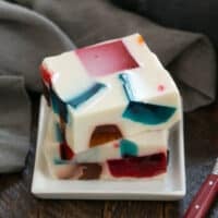 Two squares of stained glass jello on a square white plate.
