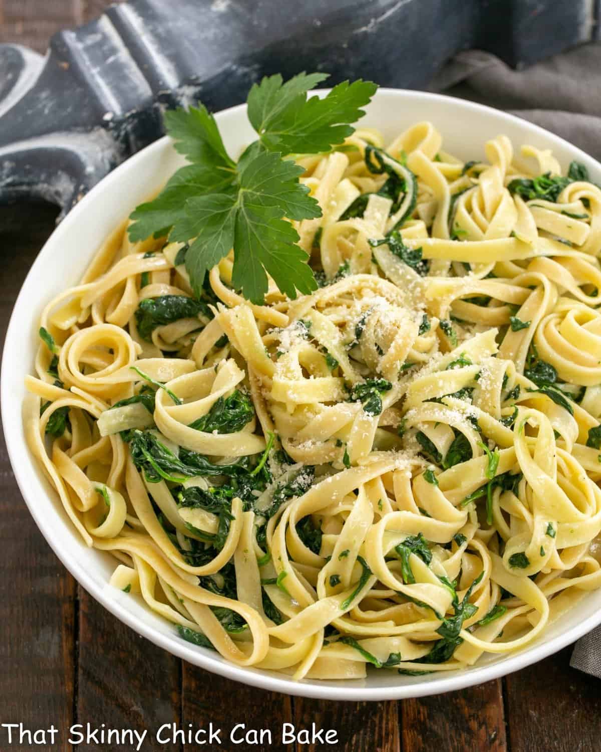 Overhead view of fettuccine alfredo with spinach in a white serving bowl.