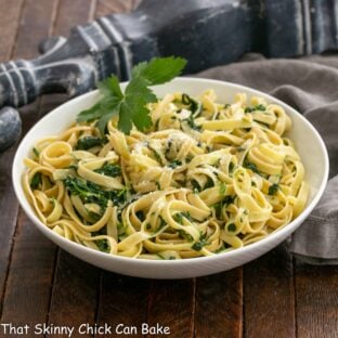 Bowl of fettuccine alfredo wih spinach in a white bowl with a parsley garnish.