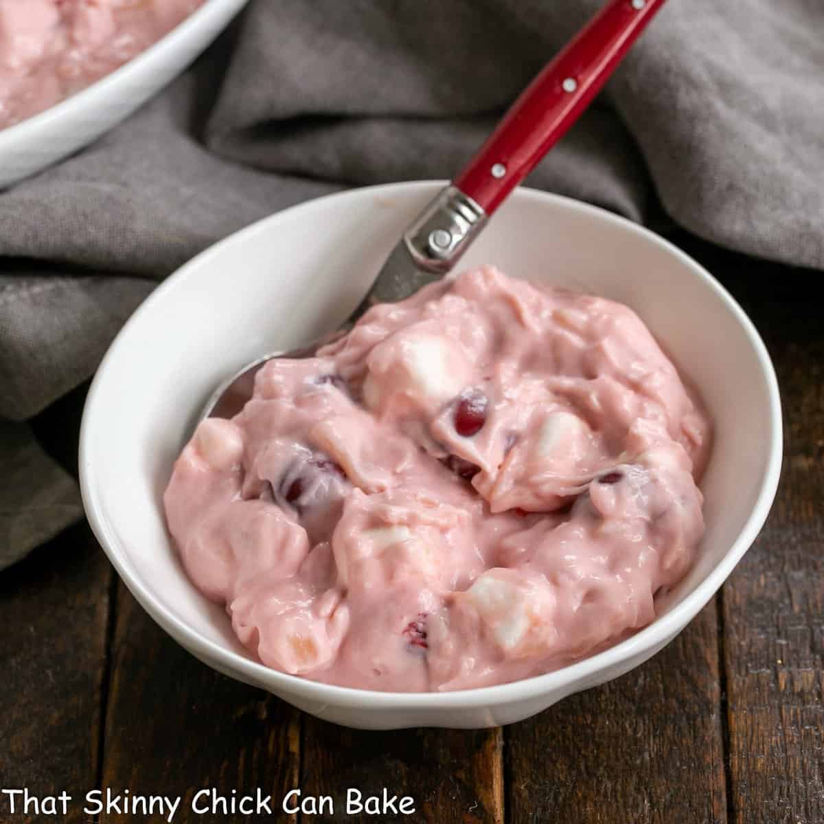 Small white bowl filled with cherry fluff salad with a red handled spoon.