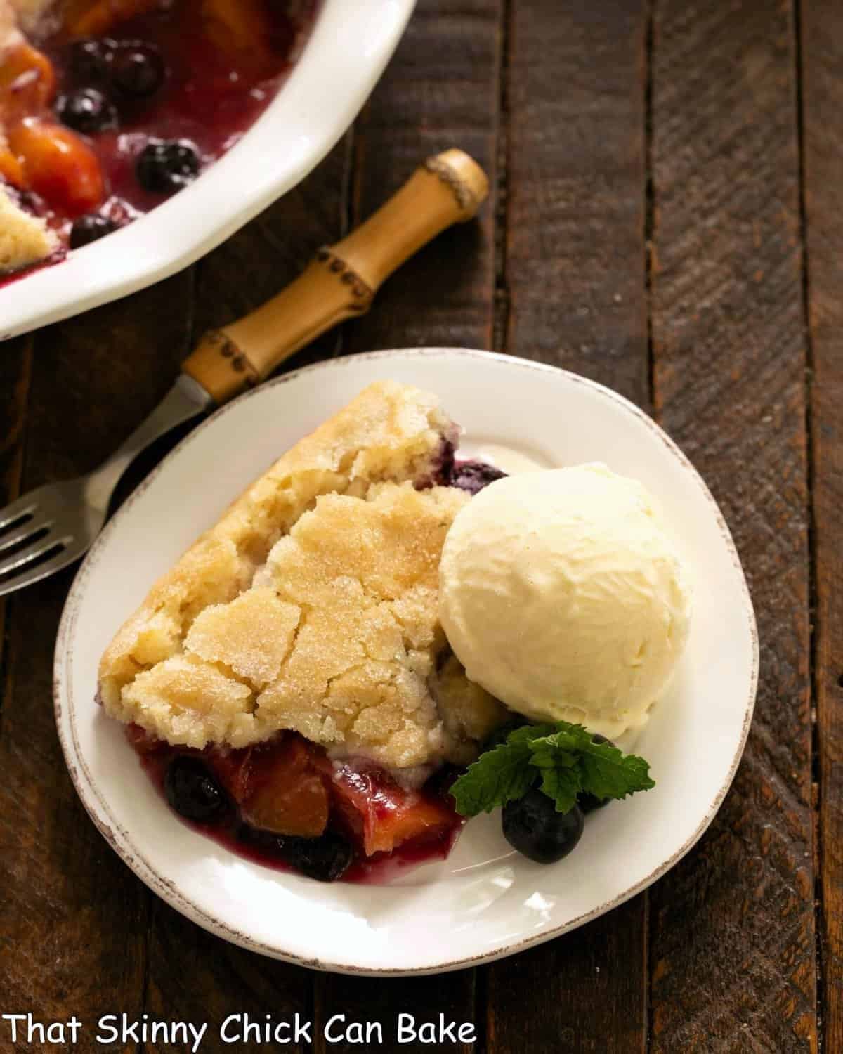 Serving of fruit cobbler with ice cream on a white plate with a fork.