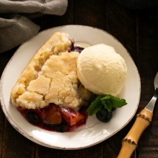 Serving of peach blueberry cobbler with a scoop of ice cream on a white dessert plate.