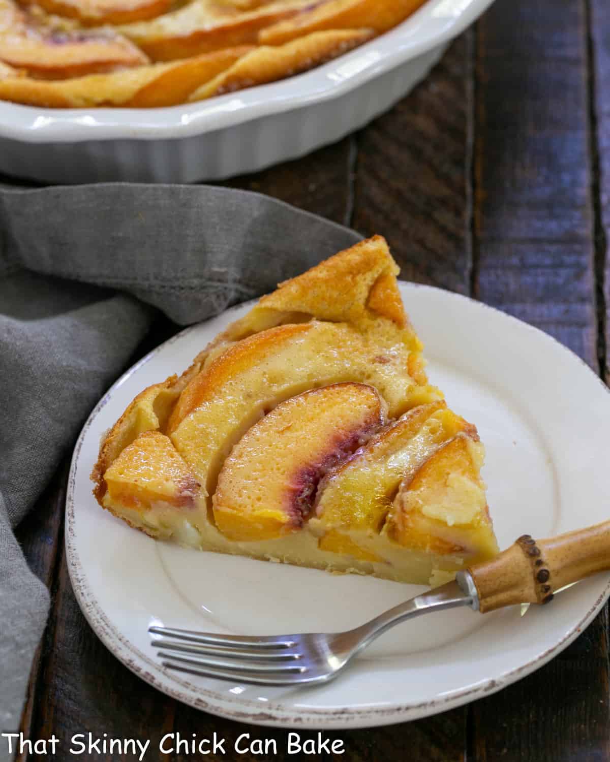 Slice of clafoutis on a white plate with a bamboo fork.