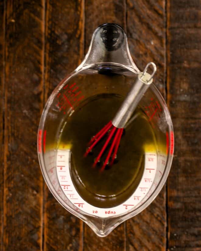 Salad dressing ingredients in a measuring cup with a whisk.