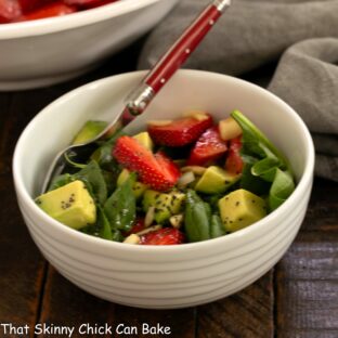 White bowl filled with spinach and strawberry salad with avocados.