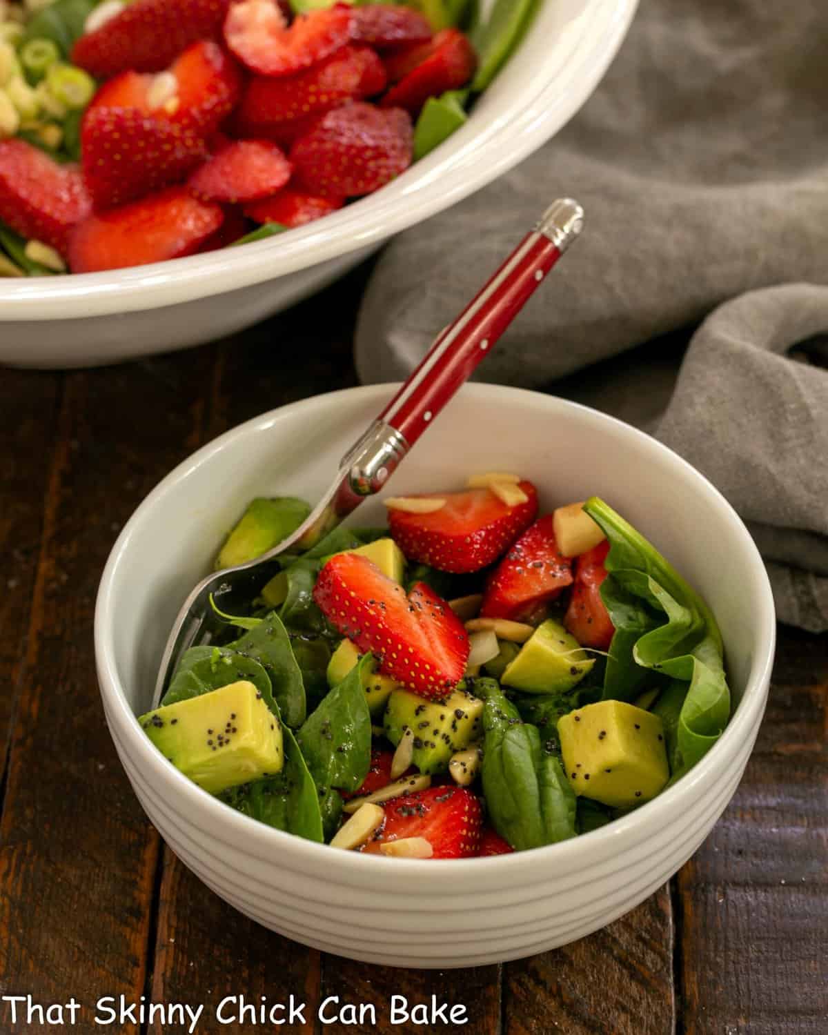 Spinach salad in a small white ceramic bowl with a red handled fork.