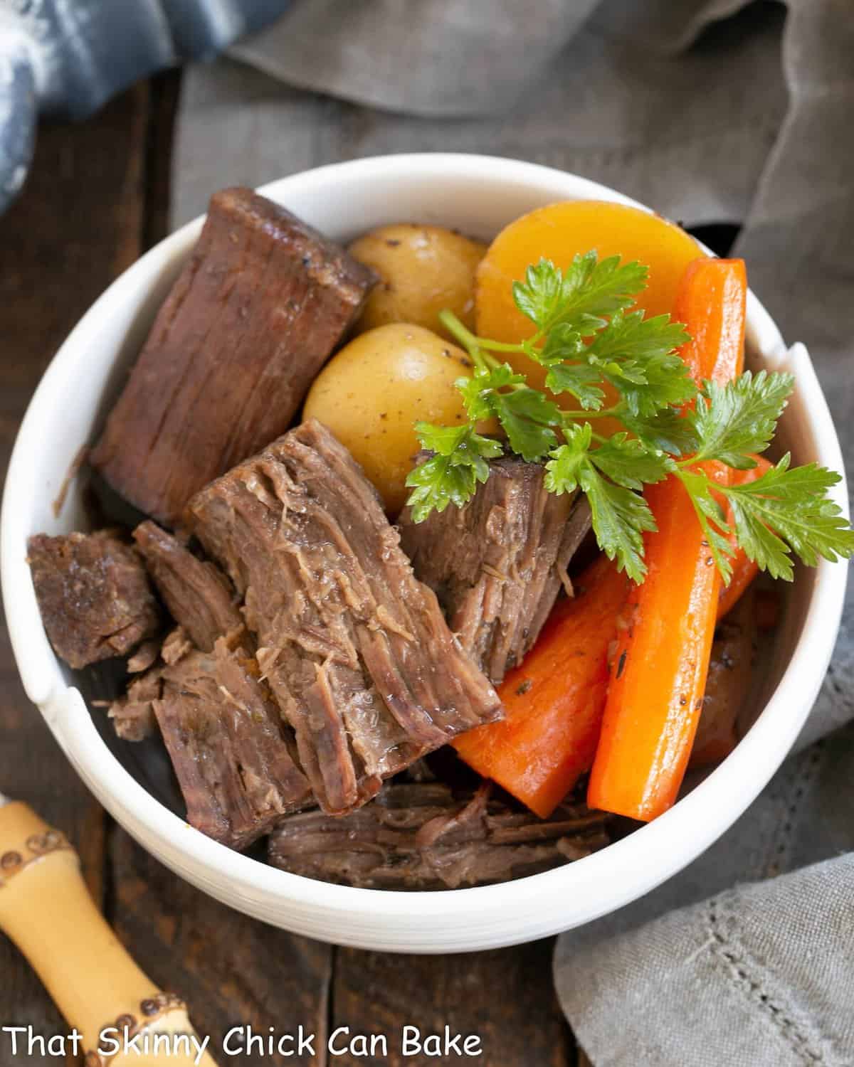 Pot roast with carrots and potatoes in a white bowl.