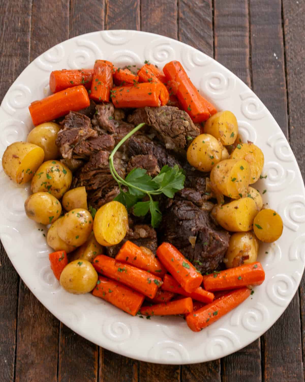 Pot roast and vegetables on a white oval platter.