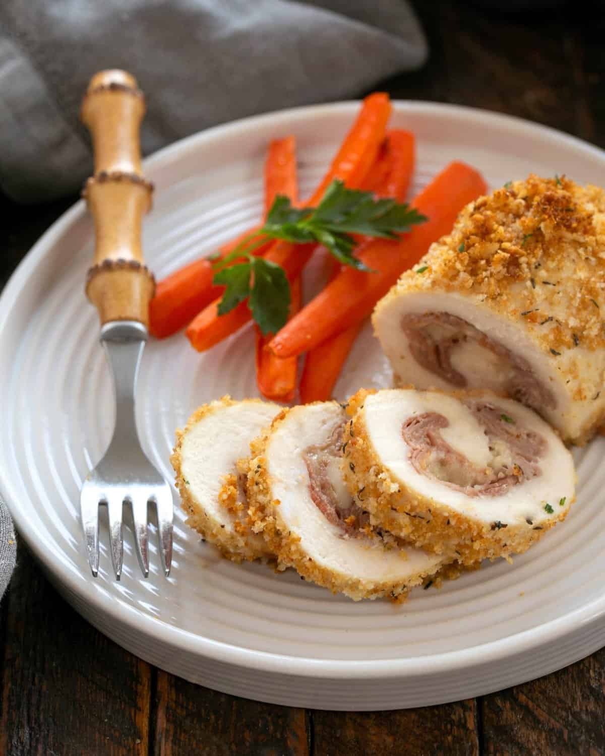 Chicken Cordon Bleu partially sliced on a white plate with carrots and a fork.